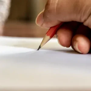 Hand holding a red pencil poised above a blank white paper.