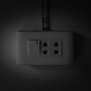 White electrical outlet with two sockets and a toggle switch on a dark wall.