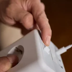 Fingers press a white power switch on a white electronic device.